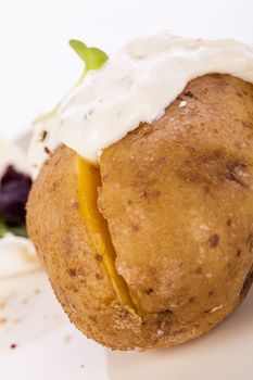 Overhead view of a healthy oven baked jacket potato with sour cream sauce garnished with endive leaves and fresh herbs