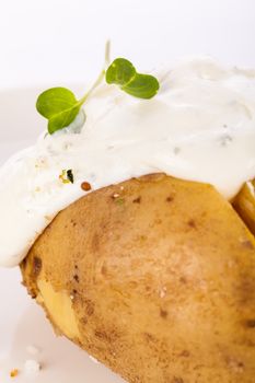 Overhead view of a healthy oven baked jacket potato with sour cream sauce garnished with endive leaves and fresh herbs