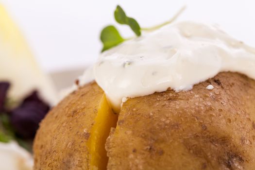 Overhead view of a healthy oven baked jacket potato with sour cream sauce garnished with endive leaves and fresh herbs