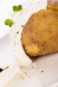 Overhead view of a healthy oven baked jacket potato with sour cream sauce garnished with endive leaves and fresh herbs
