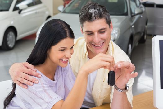 Smiling couple holding their new car key at new car showroom