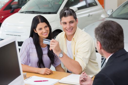 Smiling couple holding credit card to buy a car at new car showroom