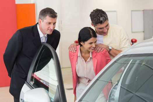 Car dealer showing the interior of a car to a couple at new car showroom
