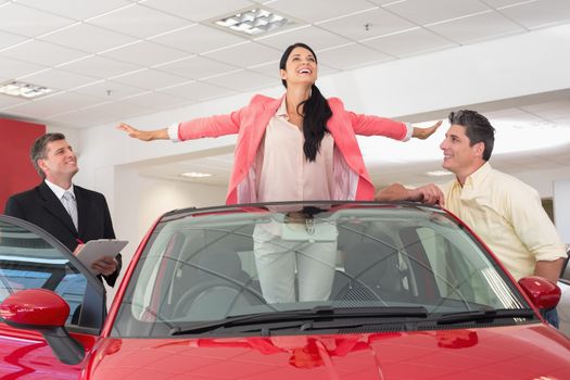 Woman having fun in her new red convertible at new car showroom