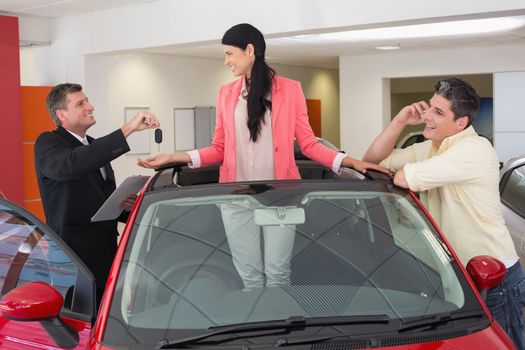 Cheerful woman standing in red cabriolet at new car showroom