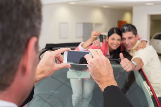 Businessman taking picture of the couple in their new car at new car showroom