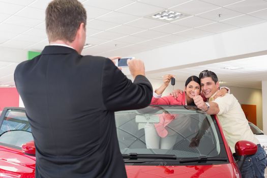 Businessman taking picture of the couple in their new car at new car showroom