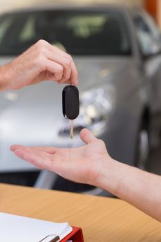 Salesman giving a customer car keys at new car showroom