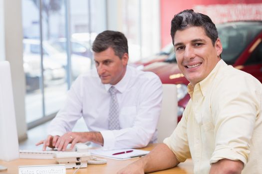 Smiling customer looking at camera at new car showroom