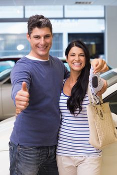 Smiling couple holding their new car key at new car showroom