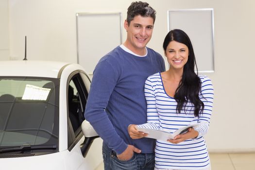 Smiling couple holding a booklet while looking at camera at new car showroom