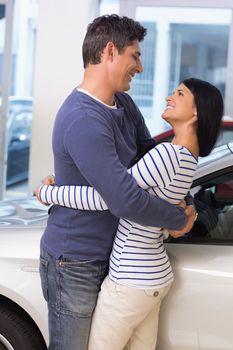 Smiling couple hugging and smiling at new car showroom