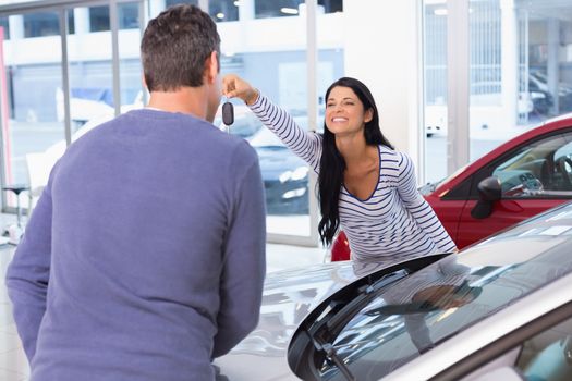 Smiling woman holding her new key at new car showroom