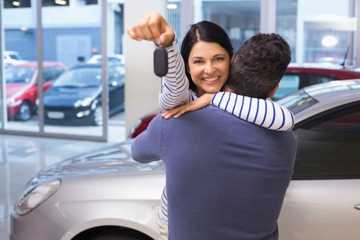 Smiling couple hugging and holding their new key at new car showroom