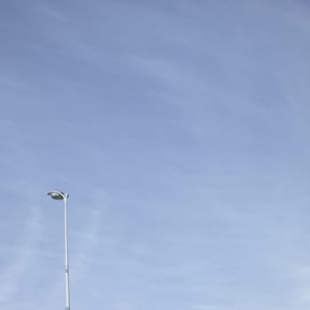Streetlight towering up into a cloudy blue sky