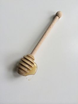 Puddle of honey and wooden dipper on white surface
