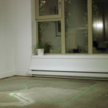 Green tape on a concrete floor in the shape of a baby grand piano in the interior of an empty condominum 
