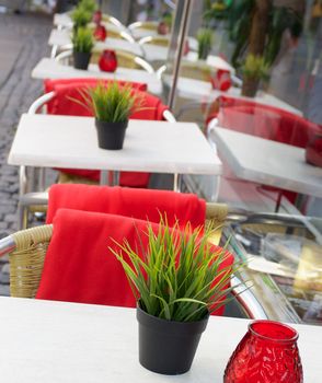 Elegant Street Cafe with Green Grass Pots, Candles and Red Plaids on Stainless Steel Chairs Outdoors. Focus on Foreground