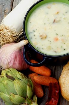 Healthy Artichoke Creamy Soup with Leek, Carrot, Garlic and Cheese in Dark Blue Pannikin closeup on Rustic Wooden background. Top View