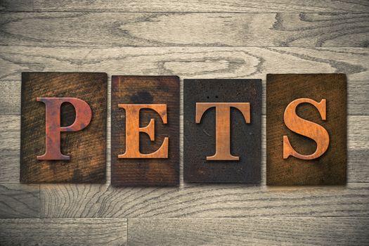 The word "PETS" theme written in vintage, ink stained, wooden letterpress type on a wood grained background.