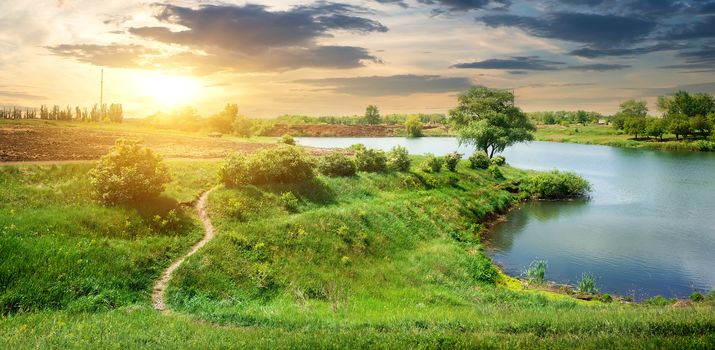 Footpath near calm river in spring at sunrise