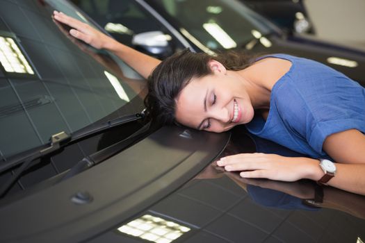 Smiling woman hugging a black car at new car showroom