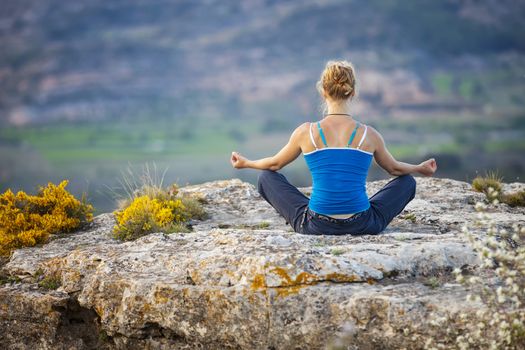 Young woman sitting on a rock and enjoying valley view. Girl sits in asana position.