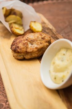 Succulent cooked beef burger with potato on a wood plate.