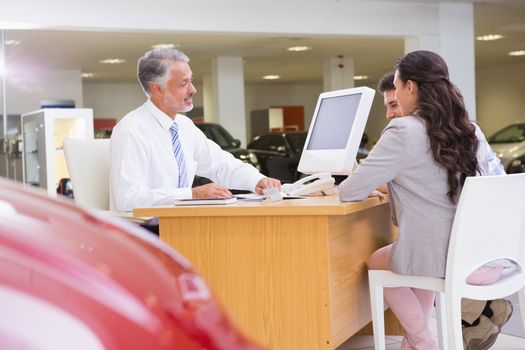 Salesman speaking with a smiling couple at new car showroom