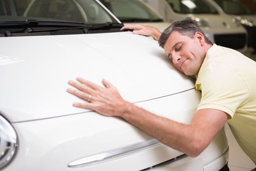 Smiling man hugging a white car at new car showroom