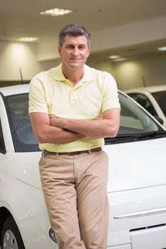 Smiling customer leaning on car with arms crossed at new car showroom