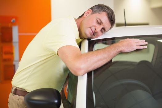 Smiling man hugging a white car at new car showroom