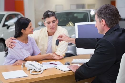 Salesman giving car keys to a couple at new car showroom