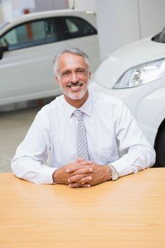 Happy businessman sitting at his desk at new car showroom