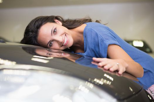 Smiling woman hugging a black car at new car showroom