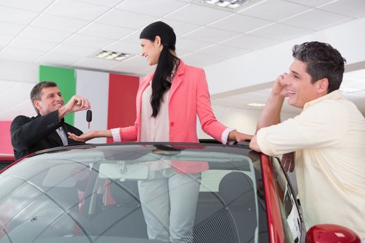 Cheerful woman standing in red cabriolet at new car showroom