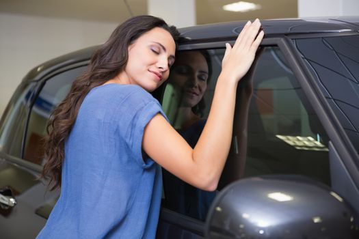 Smiling woman hugging a black car at new car showroom