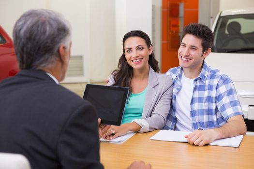 Smiling couple talking with a car dealer at new car showroom