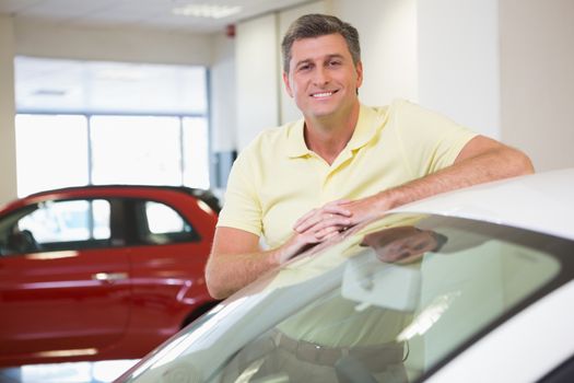 Smiling customer leaning on car at new car showroom