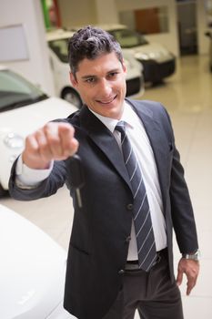 Salesman standing while offering car keys at new car showroom