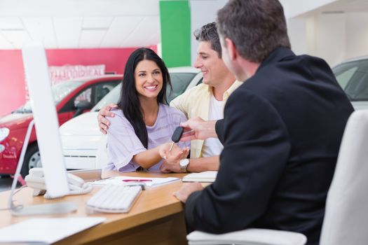 Salesman giving car keys to a couple at new car showroom