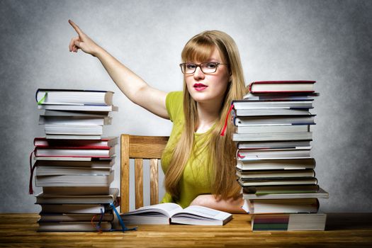 Young female teacher at a table with books pointing the finger back