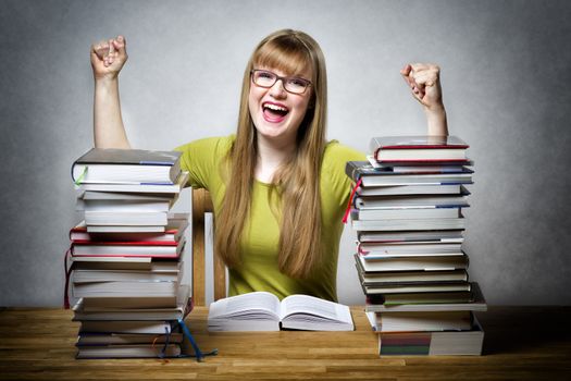 young happy schoolgirl with glasses and lots of books at a table