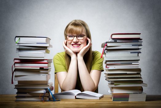 young happy female student with glasses and lots of books at a table