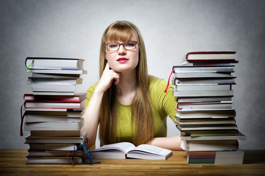 Young student with glasses sitting at a table with many books