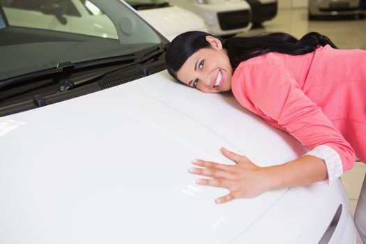Smiling woman hugging a white car at new car showroom