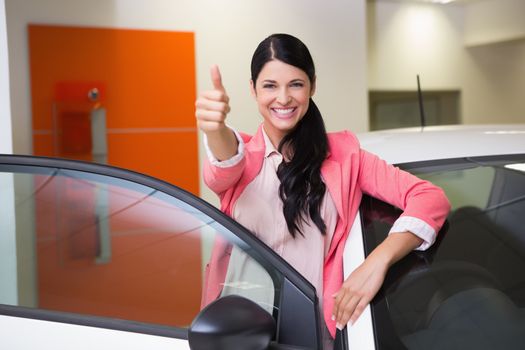Smiling customer leaning on car while giving thumbs up at new car showroom