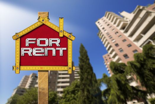 Yellow wooden meter ruler in the shape of house with text for rent. For rent real estate sign with tall and blurred buildings in the background