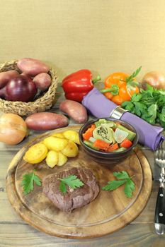 roasted ostrich steaks with baked potatoes and vegetables on a wooden board