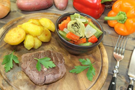 Ostrich steaks with baked potatoes and vegetables on a wooden board